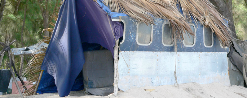 Fotograma de Lost: un refugio levantado en la playa contra el fuselaje del avión siniestrado, con techo de hojas de palmera y una lona morada haciendo de pared.