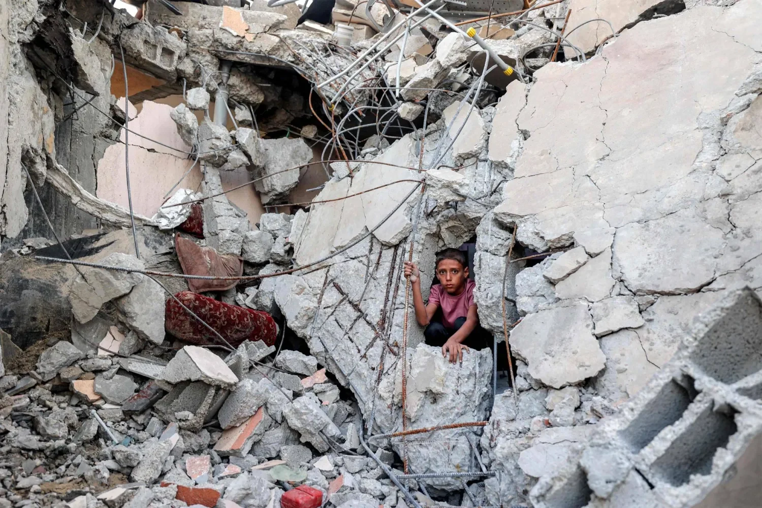 Un niño se asoma por un hueco entre bloques de hormigón y hierros retorcidos, en el interior de un edificio derrumbado.